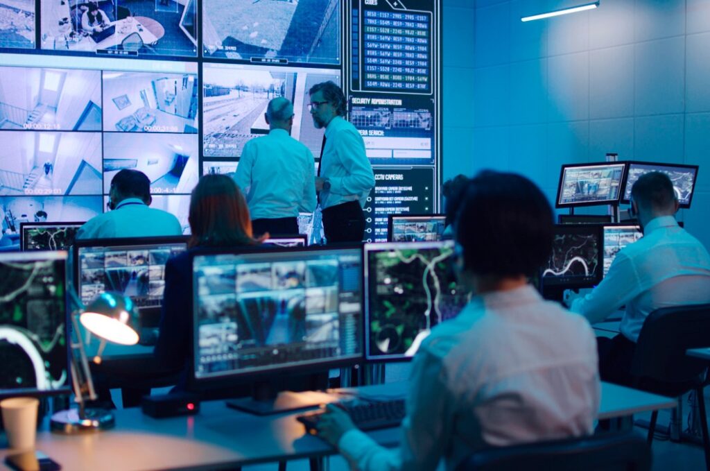 Mann arbeitet in Überwachungszentrale in der Nähe von Chefs, die Aufnahmen diskutieren